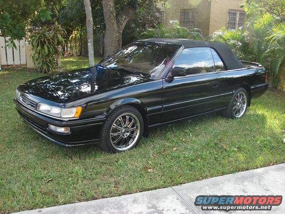 Black convertible parked on grass. Chrome wheels and black soft top
