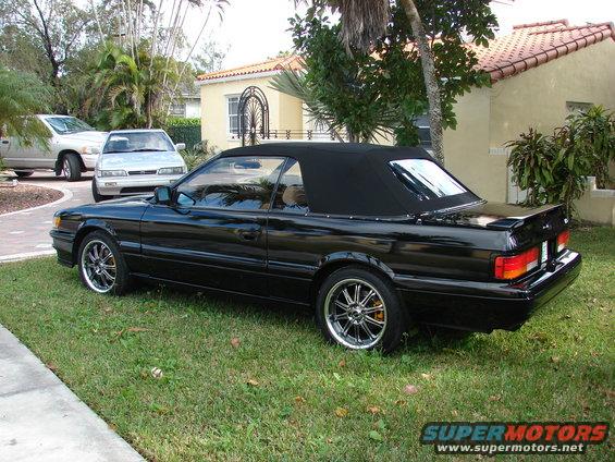 Black convertible with a black soft top, chrome wheels, and a spoiler parked on grass