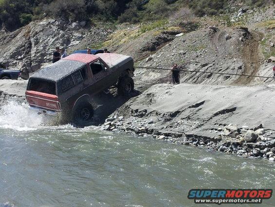 1978 Ford Bronco driving through a river with people watching