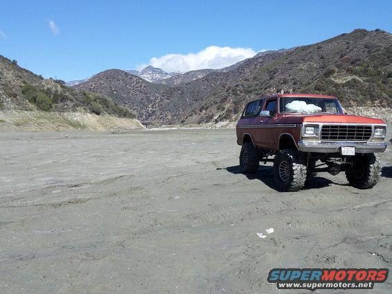 Maroon 1978 Ford Bronco with lifted suspension and large tires parked on a dry lakebed