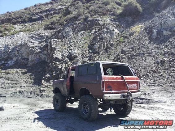 Red and maroon Ford Bronco with lifted suspension and large tires parked on a dirt road