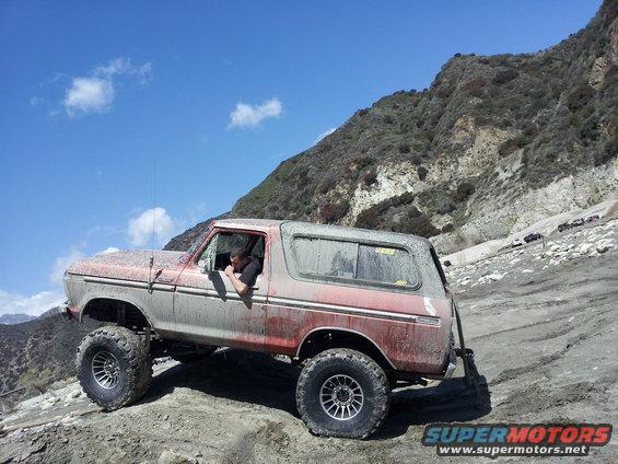 1978 Ford Bronco with mud covering its body, driving on a rocky, off-road trail