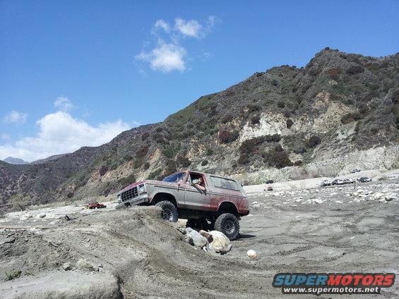 1978 Ford Bronco climbing over rocks on a dirt trail with mountains in the background