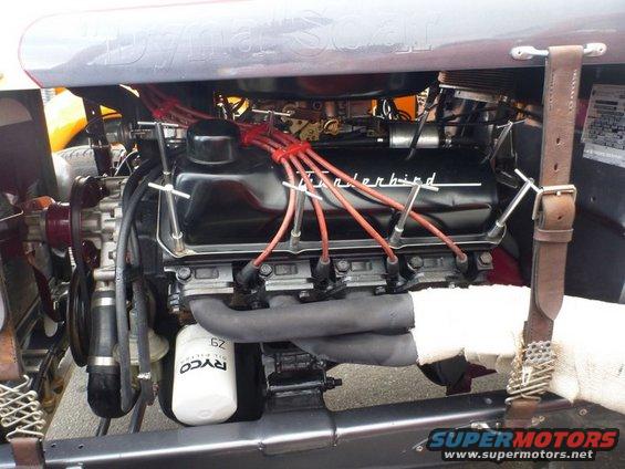 Close-up of a black engine with red spark plug wires and a silver exhaust pipe. The word "Thunderbird" is visible on the valve cover