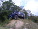 1992 Ford Bronco - Blue 1992 Ford Bronco ascends a grassy dirt mound under a cloudy sky.