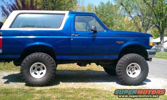 Blue 1996 Ford Bronco with a white removable top, lifted with large tires, seen from the side