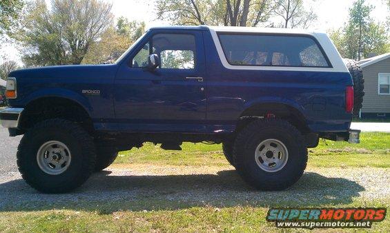 Blue 1996 Ford Bronco with white top, lifted suspension, and off-road tires parked on gravel
