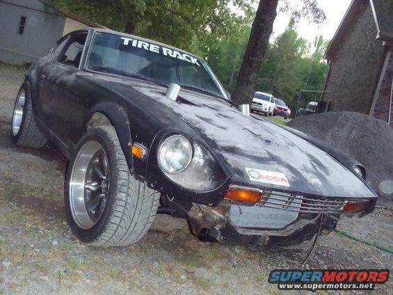 Black Nissan Fairlady Z with wide tires and 'Tire Rack' banner. Other vehicles and a pile of gravel are in the background