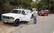 1994 Ford Bronco - Two people interact near a white Ford F-250 truck, with a red Ford Bronco parked behind it on a roadside.