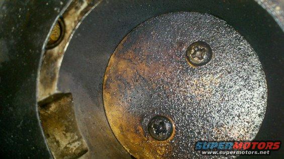 Close-up of a dirty engine cylinder with two screws visible on a circular plate