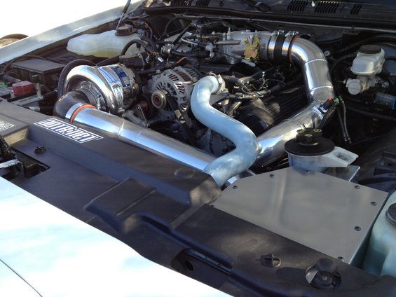 Engine bay with polished supercharger and intake piping. 'ADTR' sticker visible on plastic shroud