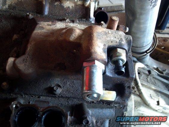 Engine block with sensors and exhaust manifold attached. Rusty metal and grime are visible