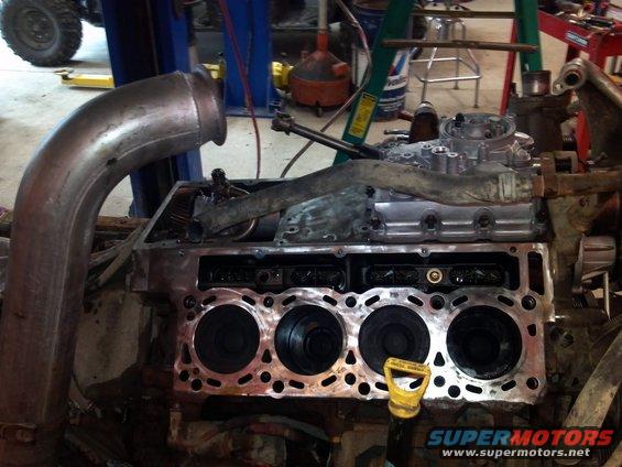 Engine block with cylinders exposed, large metal exhaust pipe on left, yellow dipstick visible