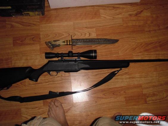 Rifle with scope and hunting knife on wooden floor