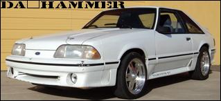 White 1987 Ford Mustang coupe with aftermarket wheels, viewed from a 3/4 front angle