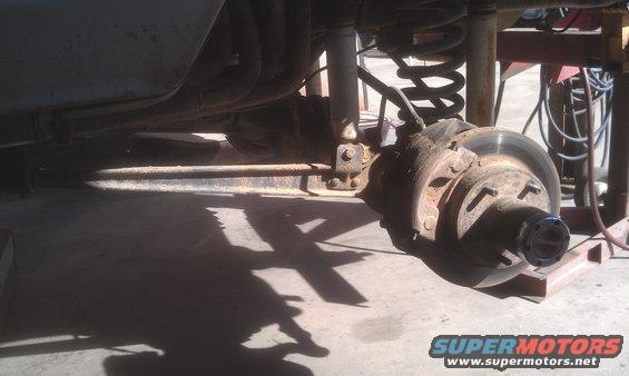 Close-up of a rusty rear axle assembly with brake rotor and suspension components
