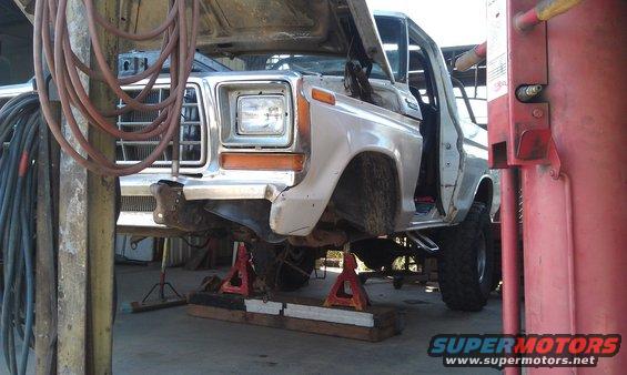 White Ford truck on jack stands, front end visible, hood open, grille and headlight assembly intact