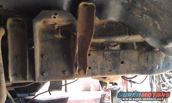 Underside view of rusty vehicle frame with suspension brackets and bolts