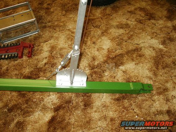 Green metal bar with silver mechanical assembly and red tool on brown carpet