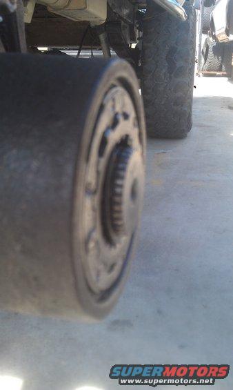Close-up of a vehicle's axle hub and tire. Another vehicle is visible in the background