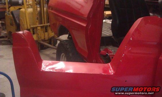 Close-up of red vehicle body panels with a yellow forklift in the background. Supermotors.net logo visible