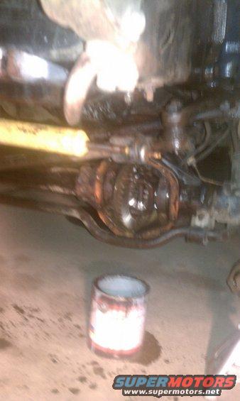 Close-up of a vehicle's rear differential and yellow shock absorber. A can sits on the floor below