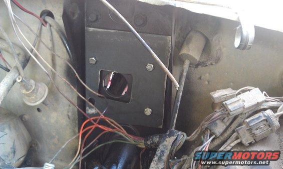 Close-up of vehicle firewall showing wiring harness and a metal plate with a circular opening