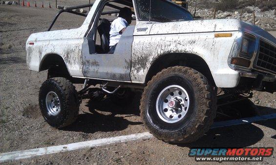 White 1978 Ford Bronco with mud splatters, lifted suspension, and off-road tires, viewed from the front three-quarter angle