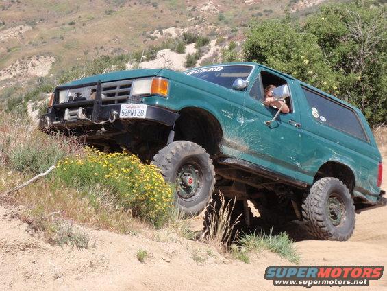 Green Ford Bronco with lifted suspension and off-road tires climbing a dirt hill