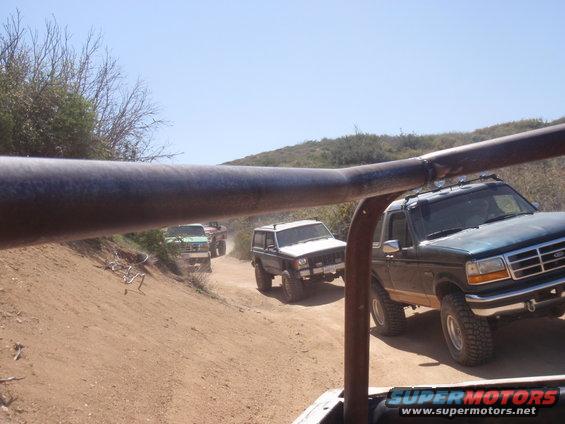Dark green 1992 Ford Bronco driving on a dirt road with other SUVs
