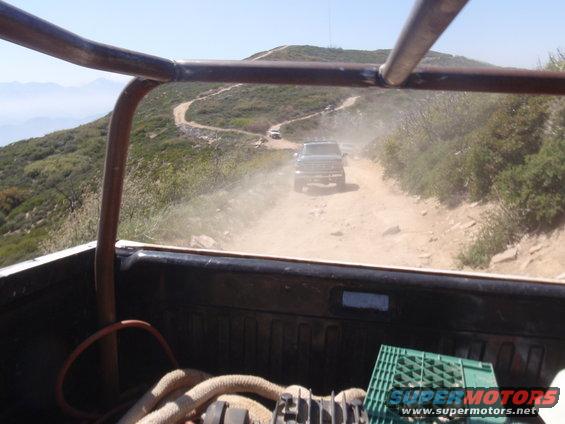 View from inside a vehicle looking at another truck driving on a dusty mountain road