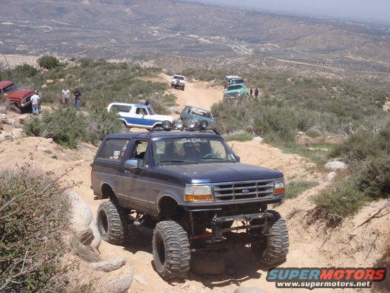 Dark blue Ford Bronco with large tires on a rocky trail