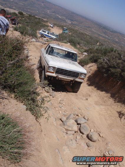 White 1978 Ford Bronco on a rocky trail, front 3/4 view. Other vehicles visible behind
