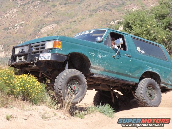 Green Ford Bronco with off-road tires climbing a dirt hill, California license plate 5ZPW128 visible