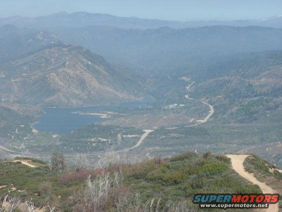 View of a lake and winding road in a mountainous, hazy landscape