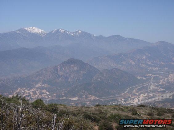 Mountain range with snow-capped peaks under a hazy blue sky, a highway winds through the valley below