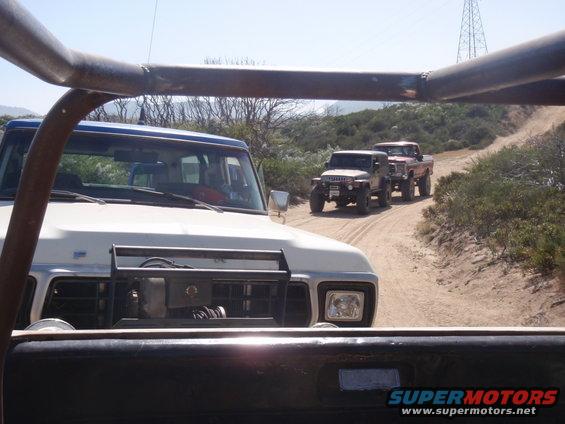 Front view of a 1978 Ford Bronco leading a convoy of off-road vehicles on a dirt road