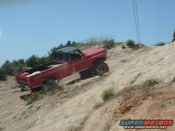 Red pickup truck with a black roof driving off-road on a dirt hill