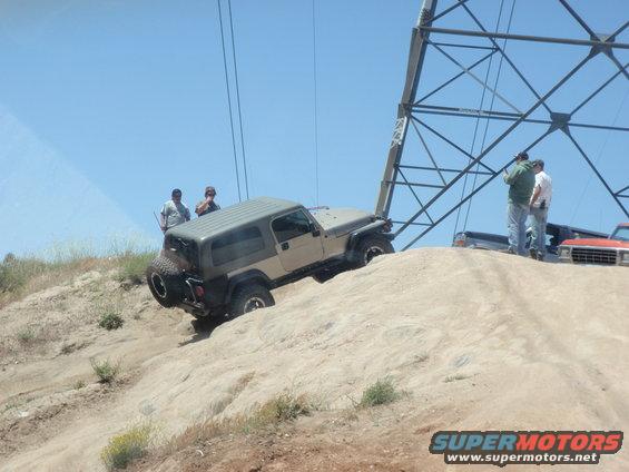 Tan Jeep Wrangler climbing a dirt hill near a power line tower