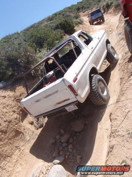 White 1978 Ford Bronco with roll cage on a steep dirt trail, another SUV behind it