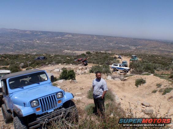 Blue Jeep Wrangler in foreground, other off-road vehicles on hill