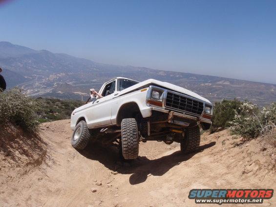 1978 Ford Bronco driving off-road on a steep dirt path with mountains in the background