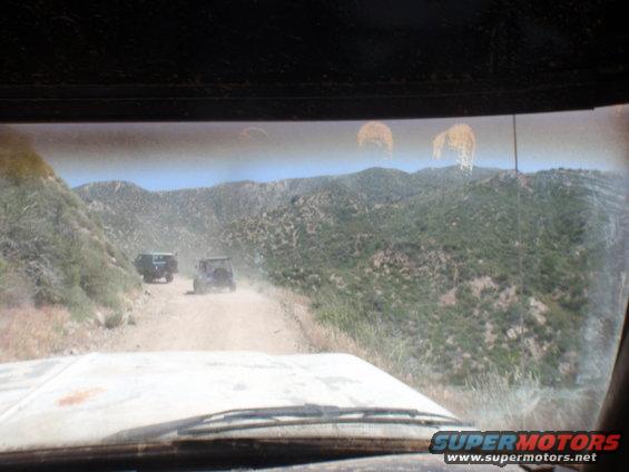 Two SUVs driving on a dusty mountain road, seen from inside another vehicle