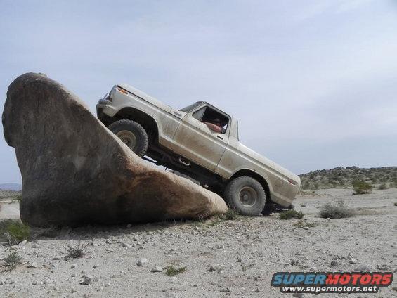 White 1978 Ford Bronco climbing a large rock in a desert landscape