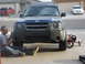 2004 Nissan Xterra - A man works on the front bumper of a blue 2004 Nissan Xterra, with a red tricycle parked beside it.