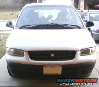 Front view of a white minivan parked in a driveway. Another car is visible to the right