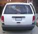 1997 Plymouth Voyager - Rear view of a white minivan parked in a driveway with the passenger side door ajar.