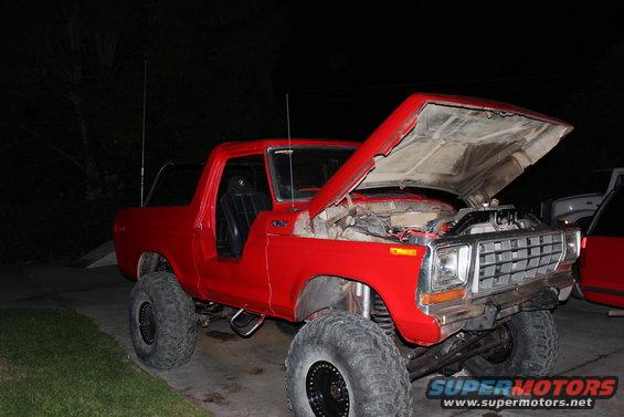 Red 1978 Ford Bronco with hood open, lifted suspension, large tires, and aftermarket exhaust pipes