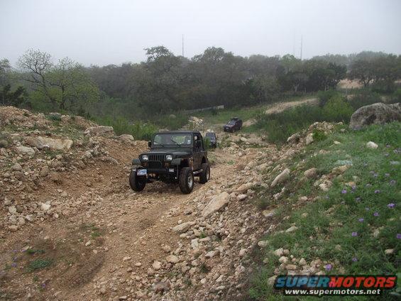 Jeep Wrangler driving up a rocky, off-road trail with two other vehicles behind it
