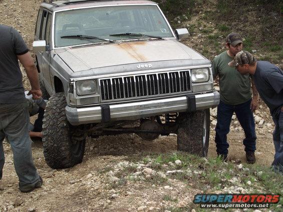 Jeep Cherokee XJ with large tires on a dirt trail, two men looking at the front